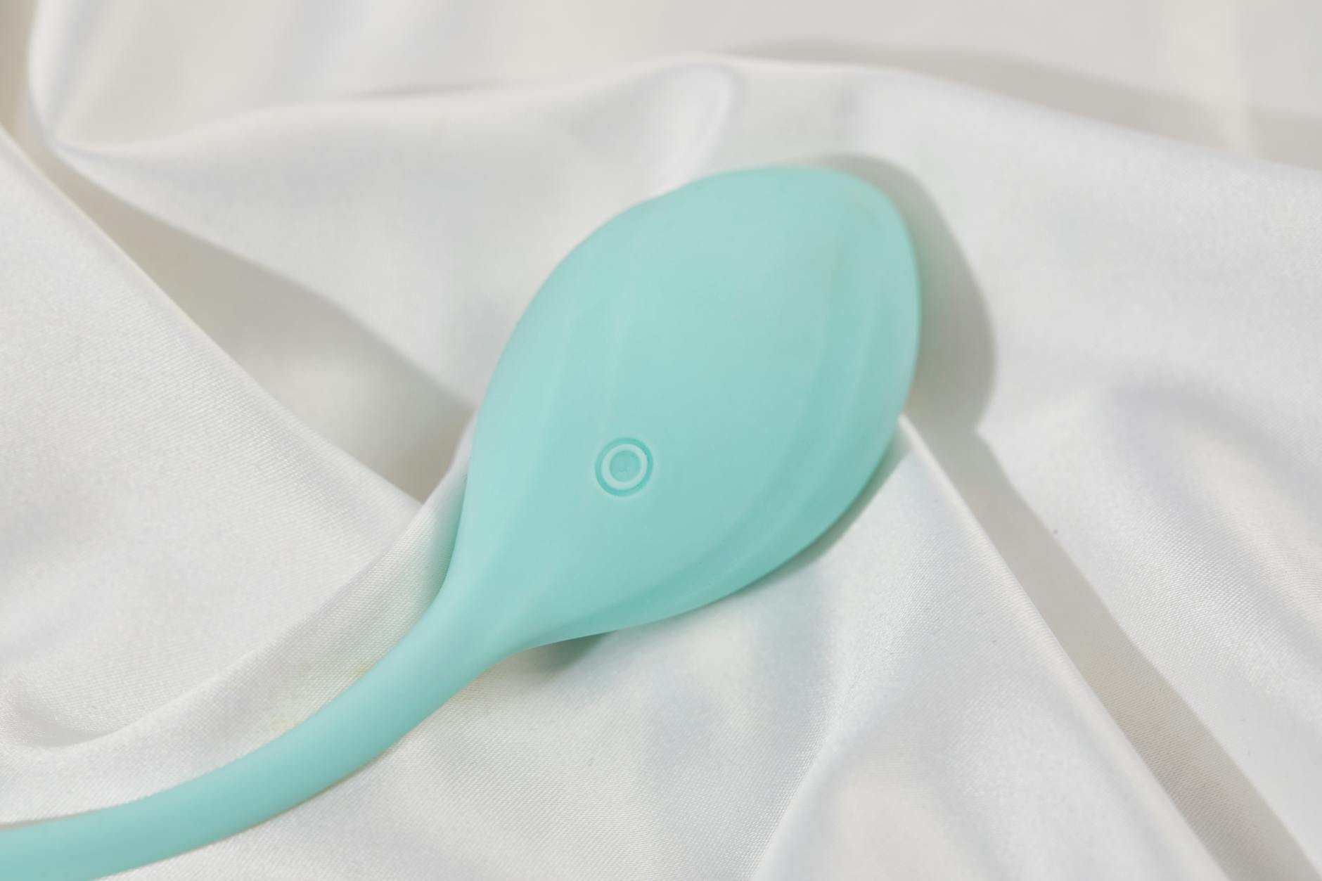 Um vibrador de limão em tons de teal sobre tecido de seda branco, mostrando design moderno e sofisticado