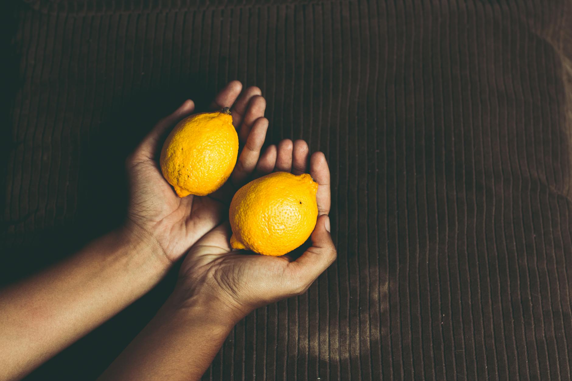 Close-up of two fresh lemons held in cupped hands, symbolizing natural pleasure and the lemon vibrator