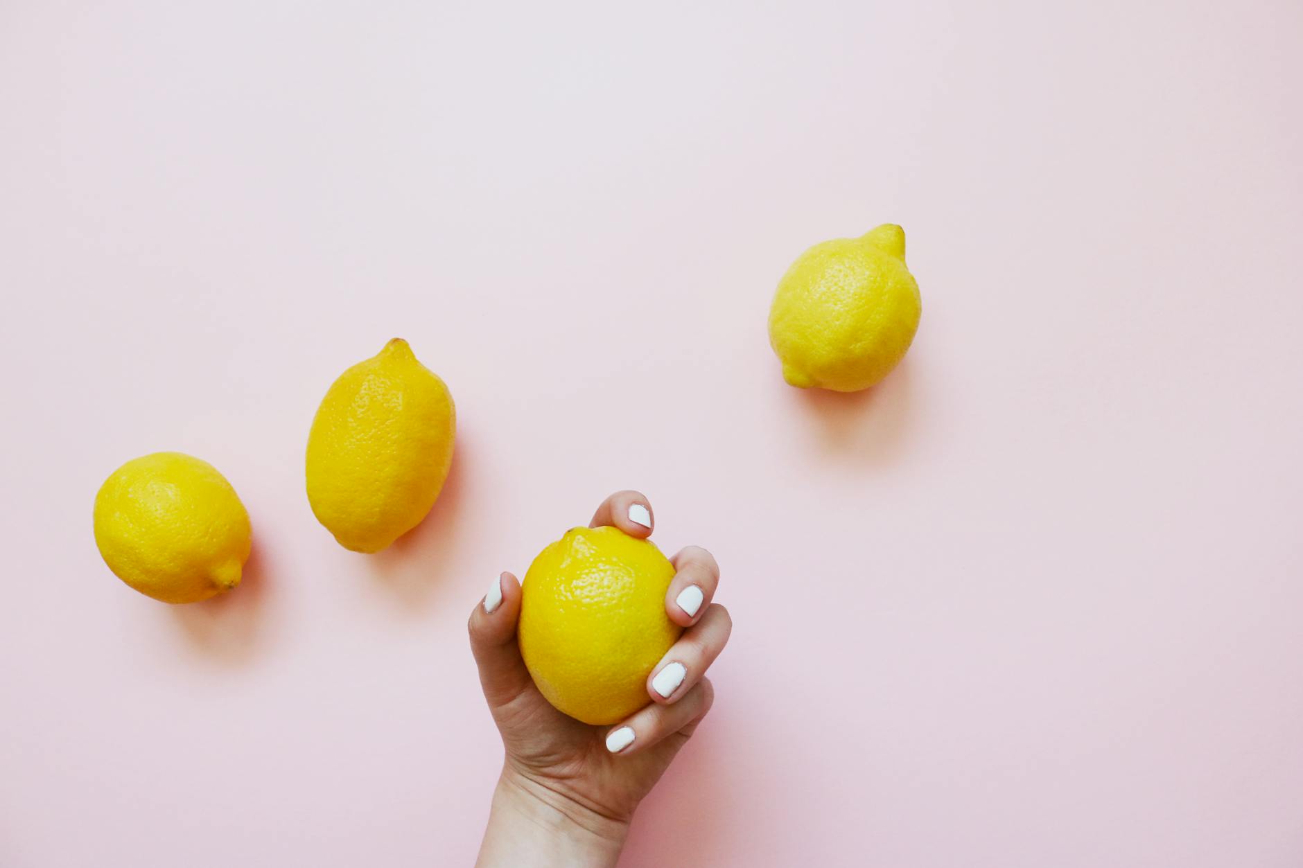 Hand with white nails holding a lemon on soft pink background