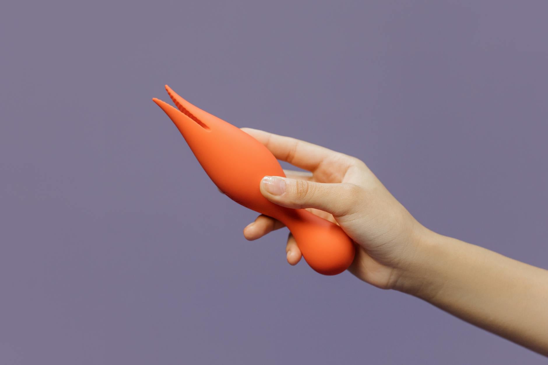 Close-up of hands holding an orange vibrator against a minimalistic purple backdrop, showcasing modern sensuality and reconnection.