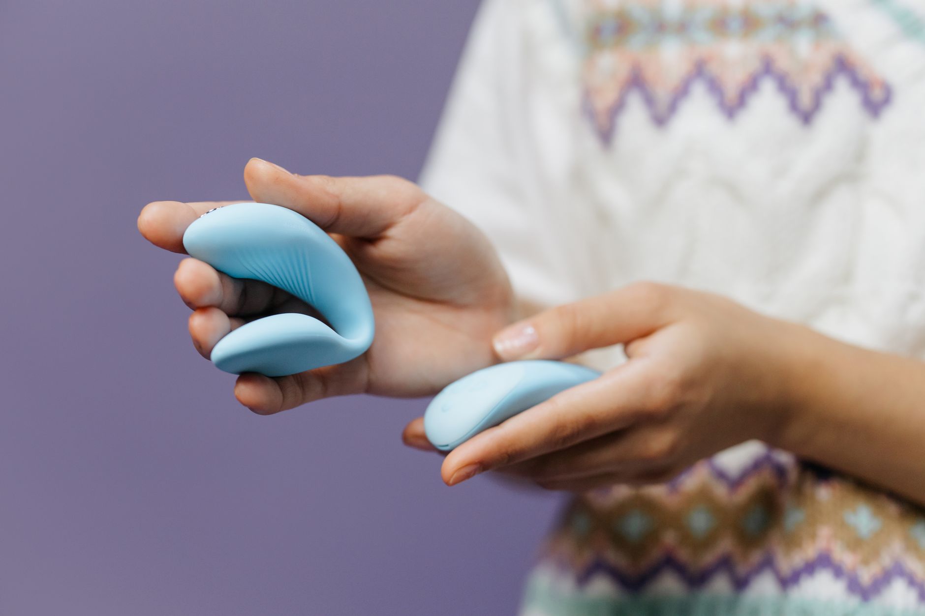 Hands holding a sleek blue vibrator against a purple background