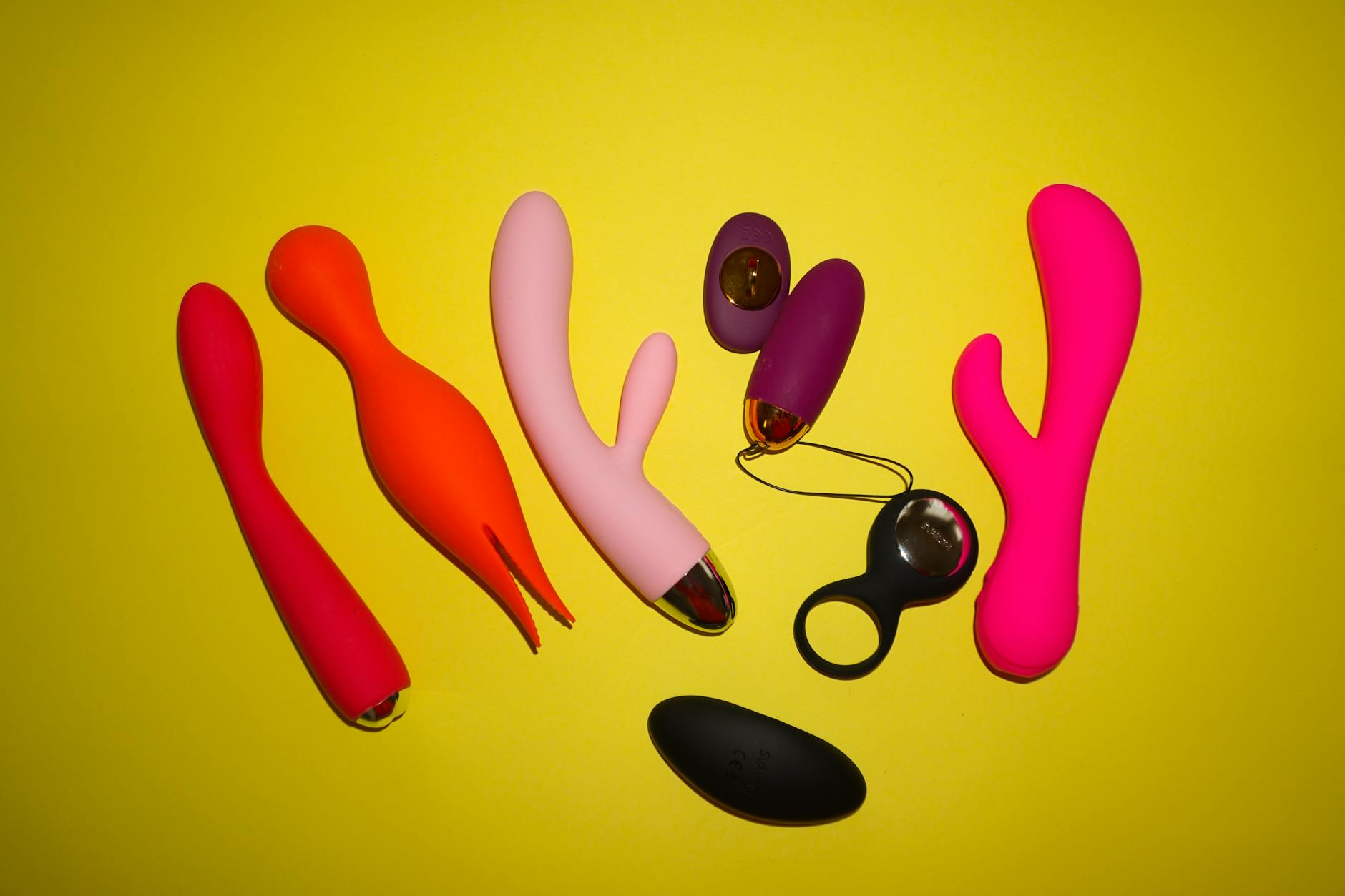 Arranjo colorido de brinquedos sexuais em fundo amarelo, mostrando variedade de possibilidades